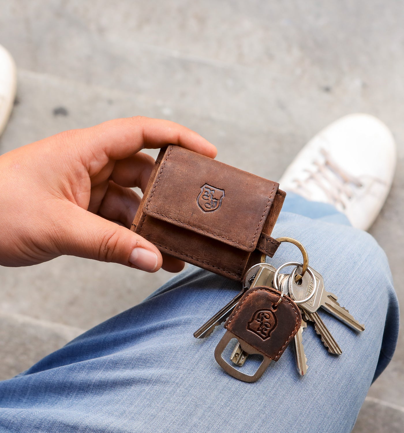 Auf dem Bild hält jemand einen kleinen braunen Leder-Schlüsselorganizer mit Hodalump-Prägung in der Hand, an dem mehrere Schlüssel samt praktischem Flaschenöffner-Anhänger befestigt sind.