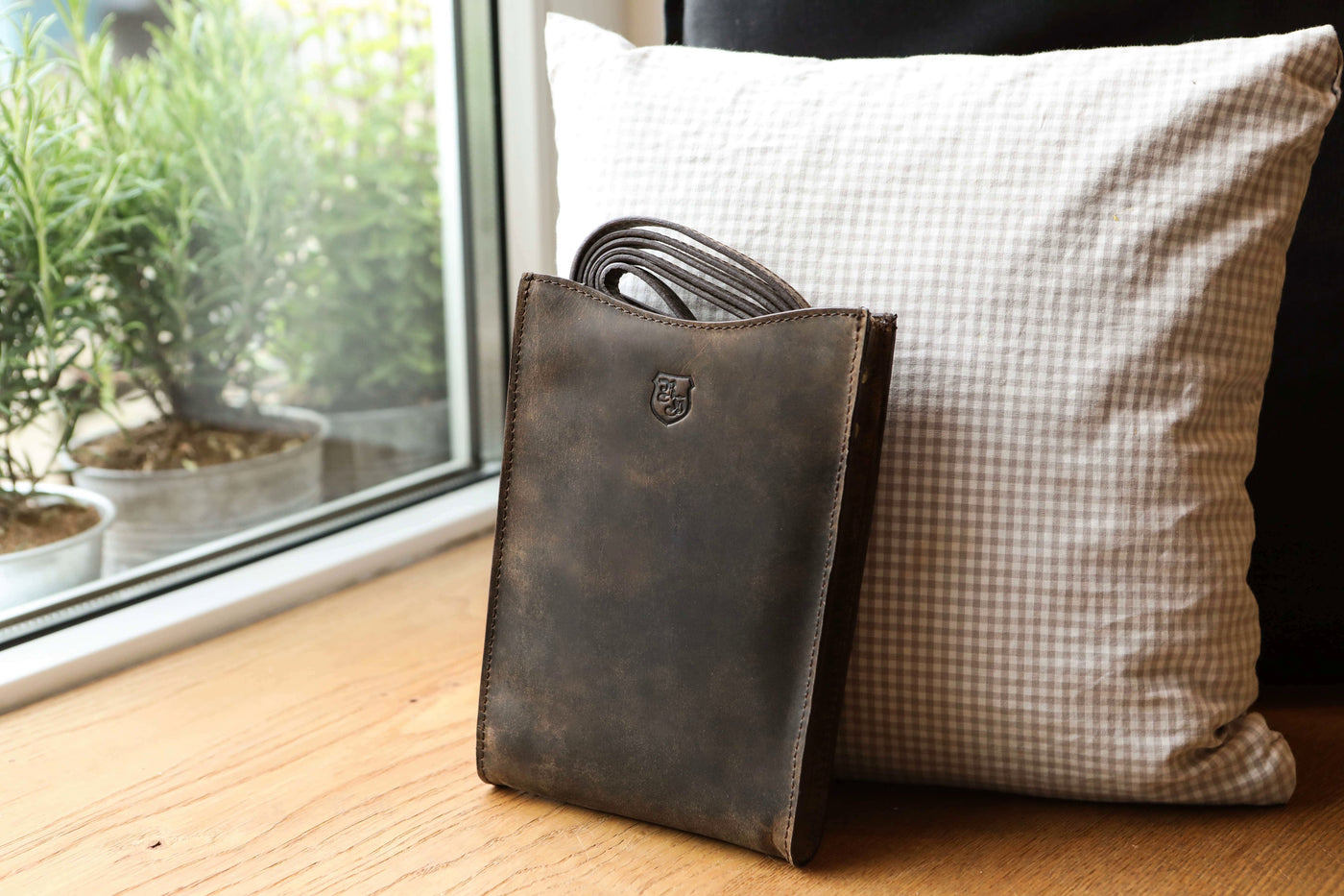 Braune Hodalump Ledertasche mit Schulterriemen auf Kissen am Fensterbrett.