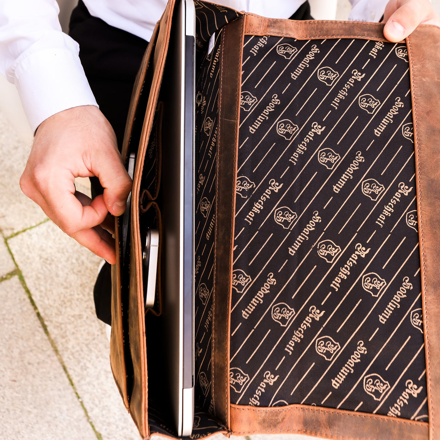 Mann steckt Laptop in braune Hodalump Laptoptasche mit bedrucktem Innenfutter.
