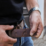 Nahaufnahme eines braunen Hodalump Ledergürtels mit geprägtem Steinbock-Motiv, getragen zu Jeans und schwarzem T-Shirt.