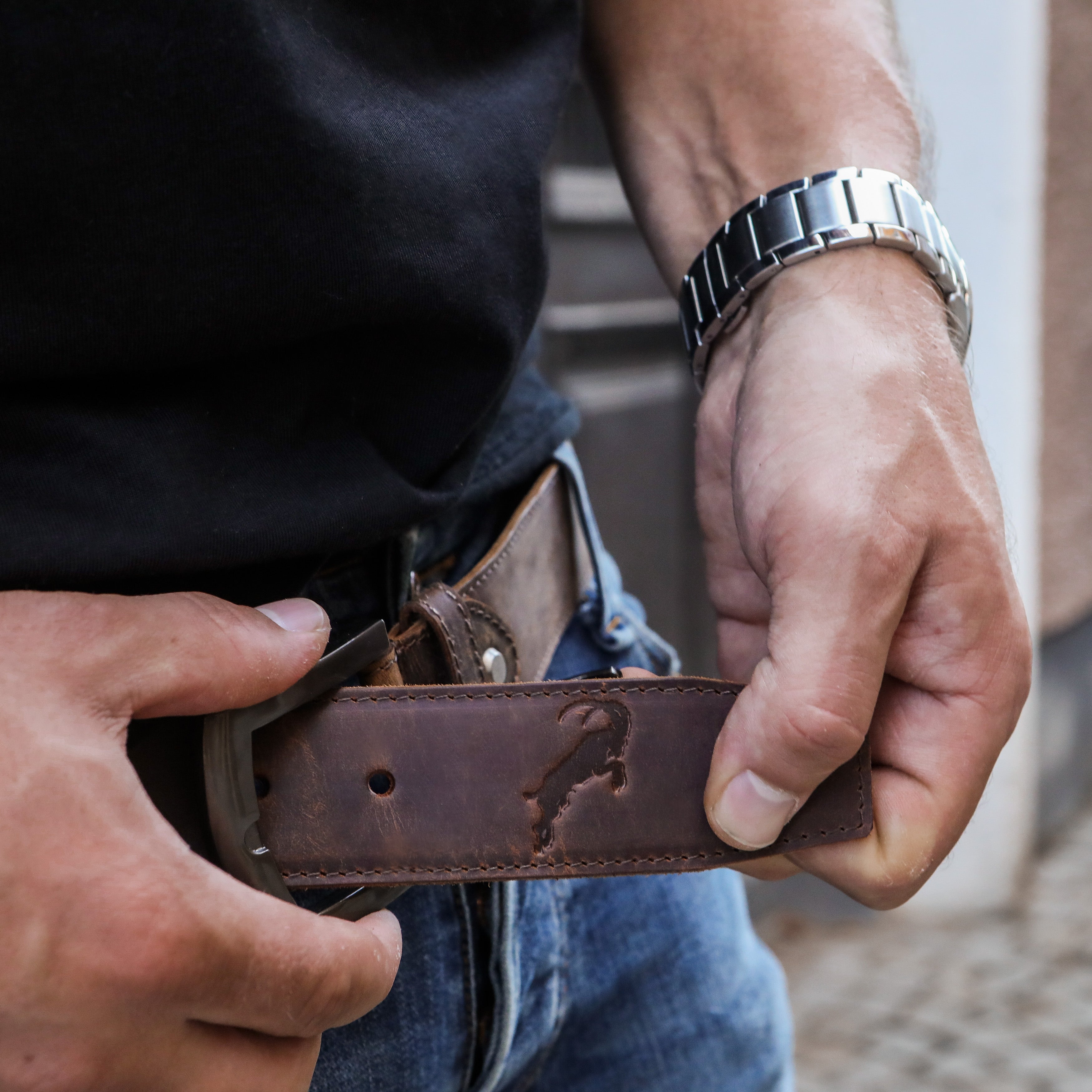 Nahaufnahme eines braunen Hodalump Ledergürtels mit geprägtem Steinbock-Motiv, getragen zu Jeans und schwarzem T-Shirt.