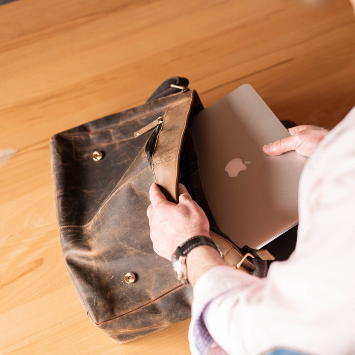 Mann steckt Laptop in braune Laptoptasche aus Leder von Hodalump – elegante Vintage Umhängetasche für Herren, ideal fürs Büro oder unterwegs.