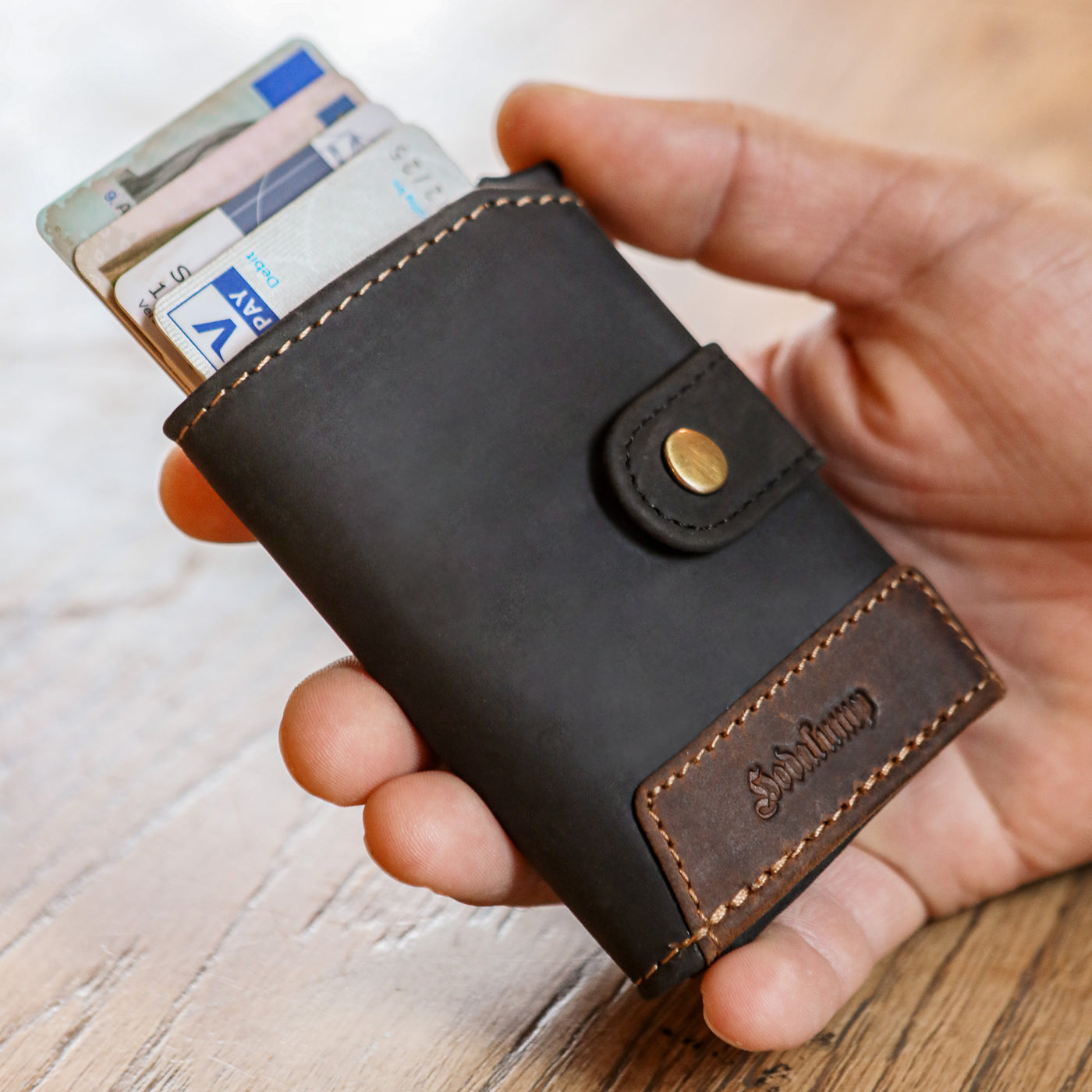 Person hält eine handgefertigte Slim Wallet Leder an einem Arbeitstisch – hochwertiges Handwerk aus echtem Leder