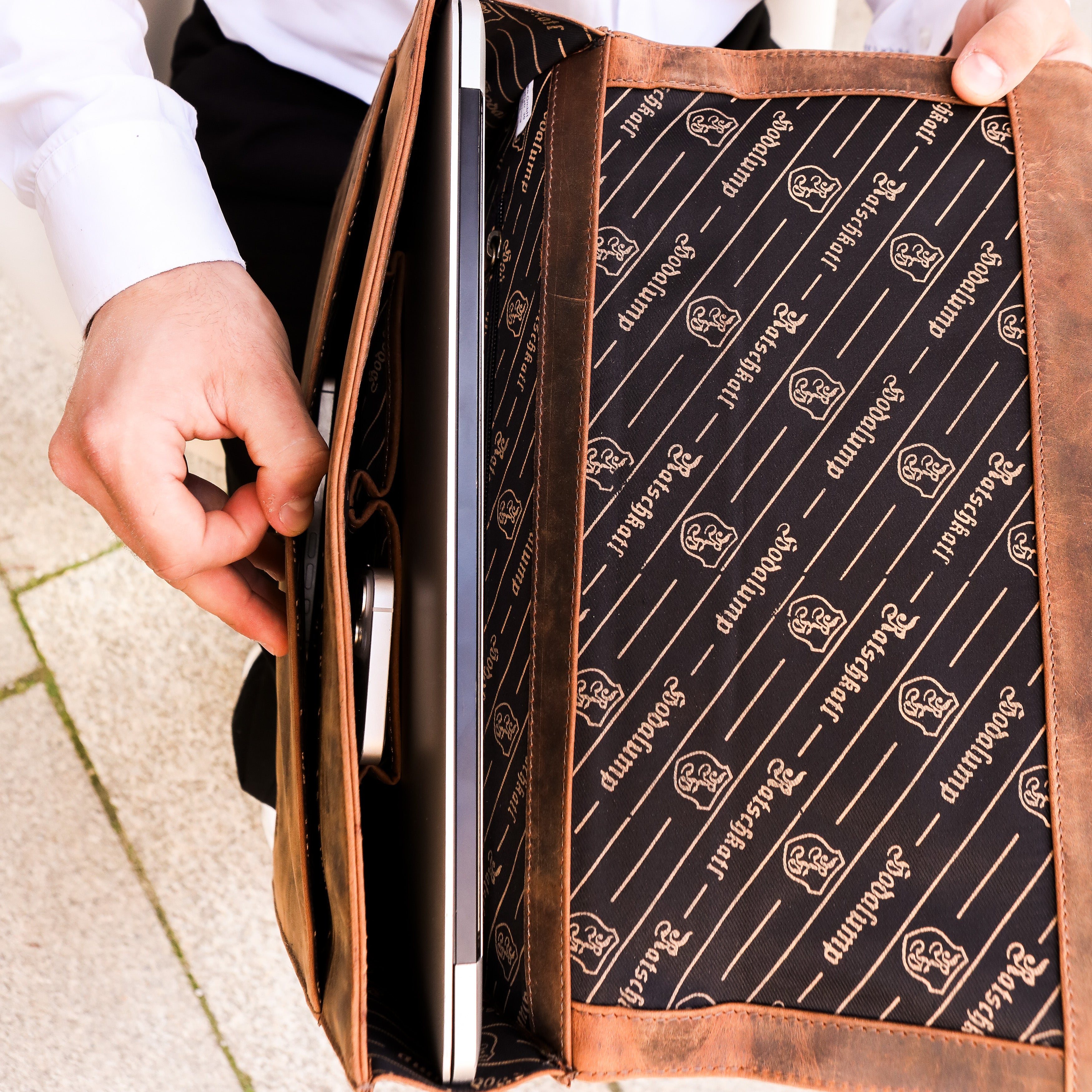 Mann steckt Laptop in braune Hodalump Laptoptasche mit bedrucktem Innenfutter.