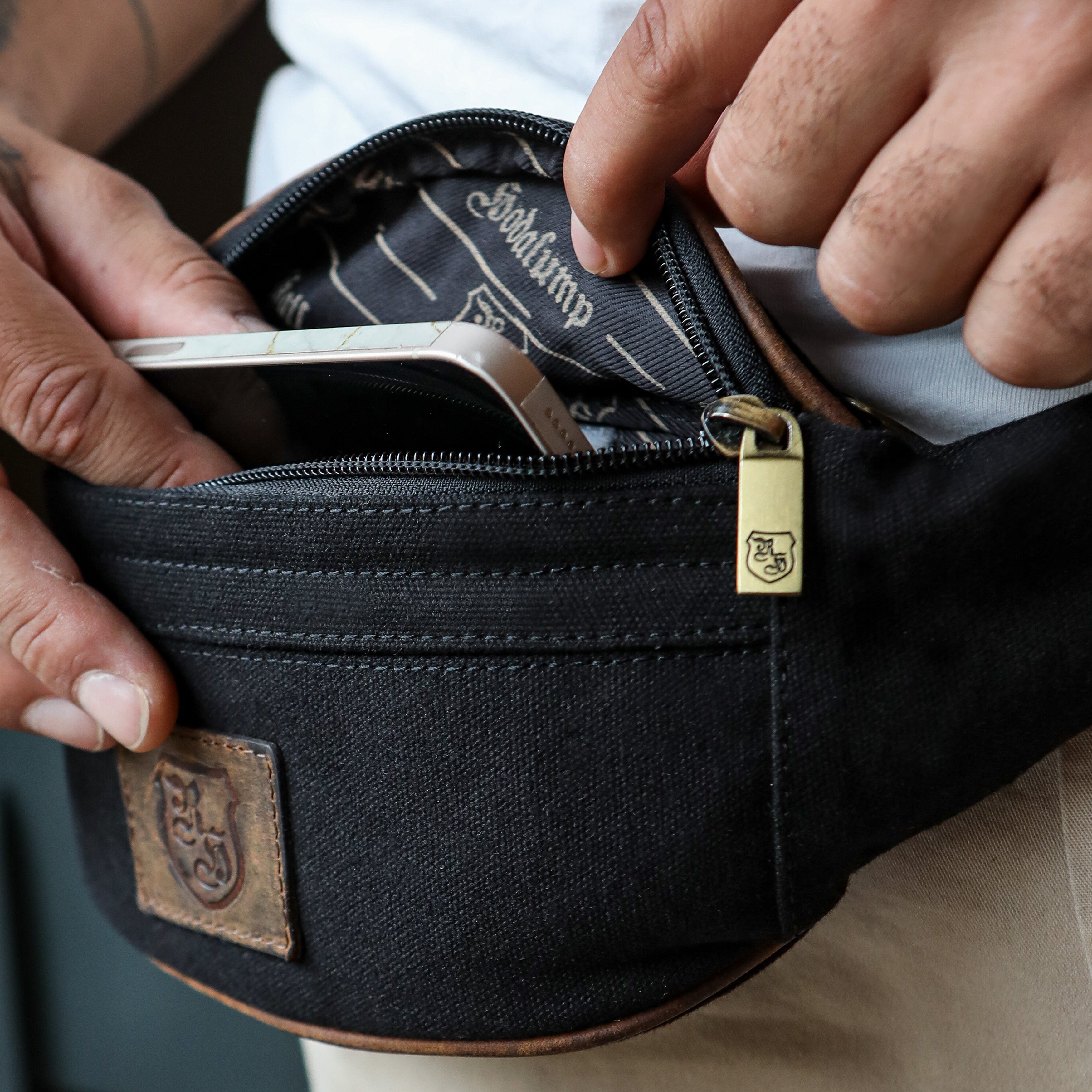 Person steckt Smartphone in schwarze Hodalump Bauchtasche mit Lederdetails.