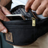 Person steckt Smartphone in schwarze Hodalump Bauchtasche mit Lederdetails.
